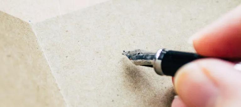 hand holding an ink pen about to write on a blank notebook